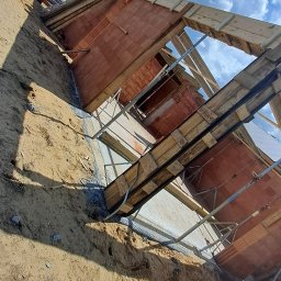 R Klawe Home firma budowlana Robert Klawe - Budowa domu z czerwonej cegły, widok z dołu na konstrukcję i niebo w Pszowie. Widoczne drewniane elementy szalunkowe i metalowe podpory.