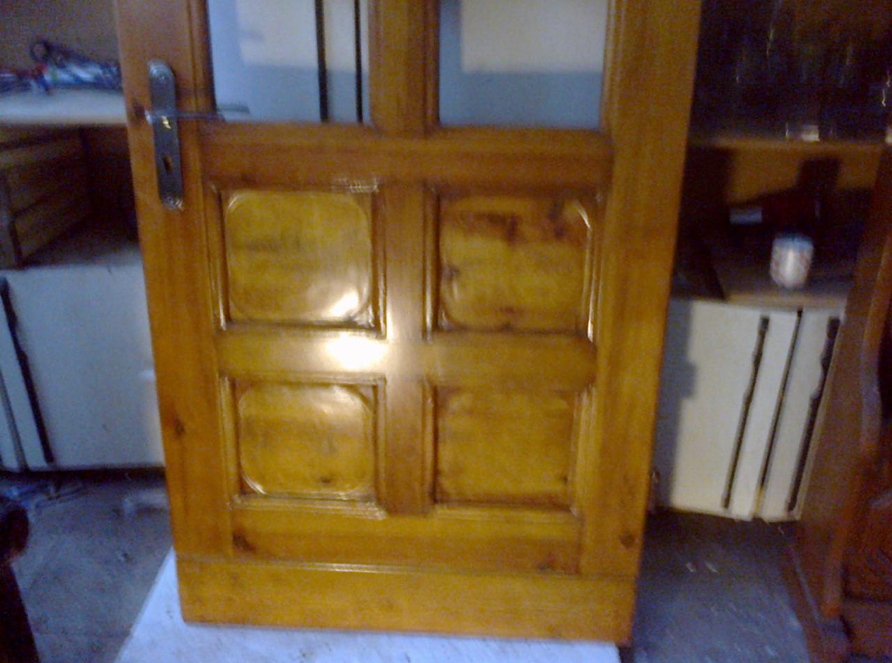 Drewniane drzwi wewnętrzne z czterema płycinami, świeżo polakierowane na złoty odcień, widoczny srebrny klucz w zamku i odbicie światła na powierzchni.