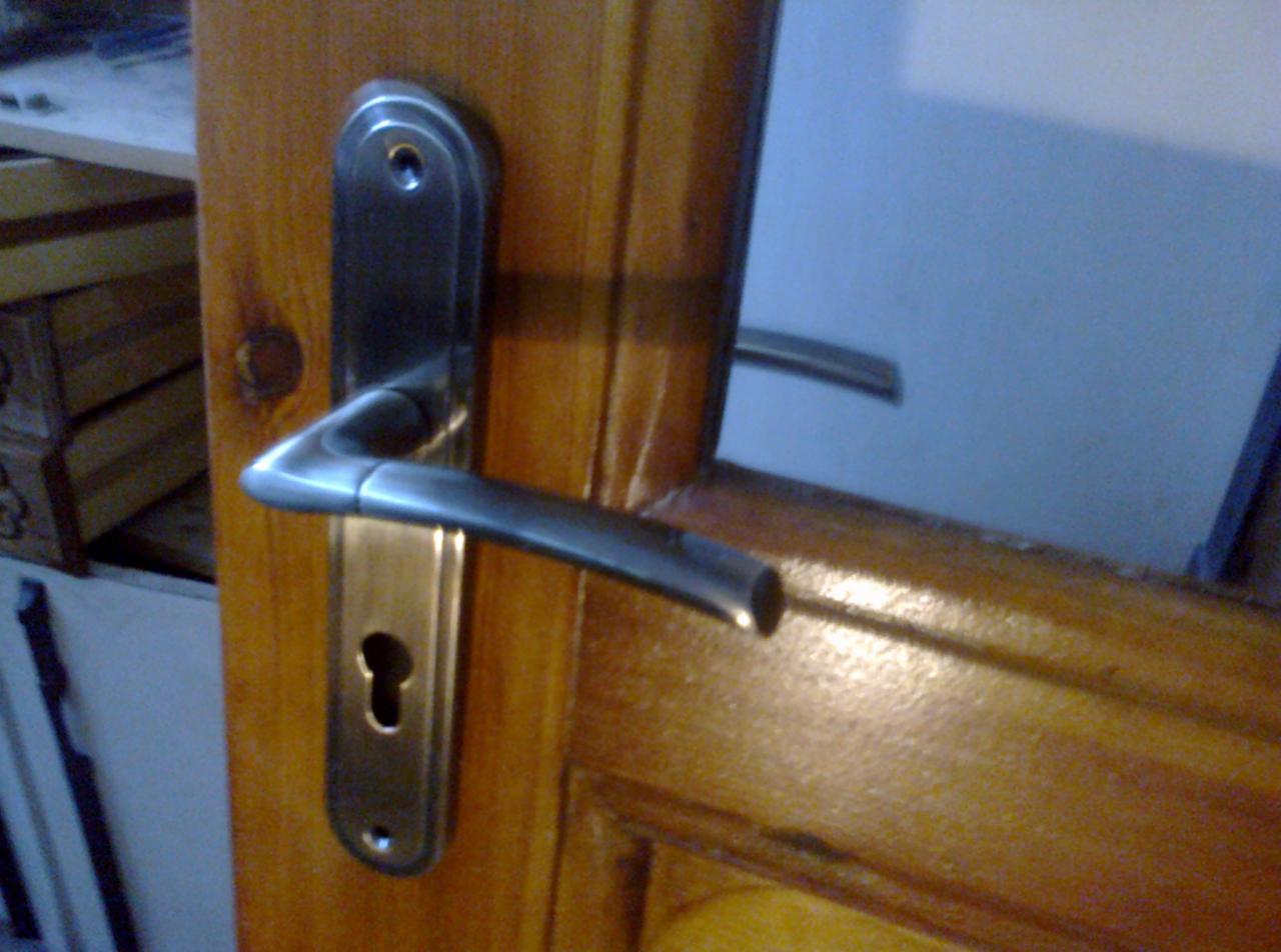 Błyszcząca, metalowa klamka z zamkiem na drewnianych drzwiach w Ornecie, widoczny zarys futryny i fragment skrzynki.