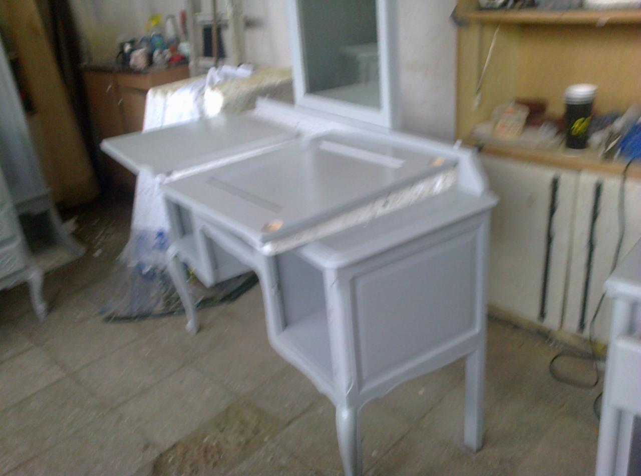 Pomalowana na szaro toaletka z lustrem i blatem roboczym w trakcie renowacji, widoczne ślady po farbie i narzędzia w tle.