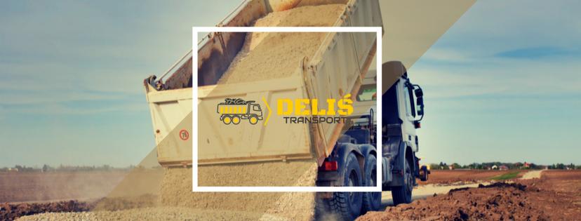 Ciężarówka z logiem firmy Delis Transport wyładowuje piasek na placu budowy, w tle widoczne pole i zabudowania.