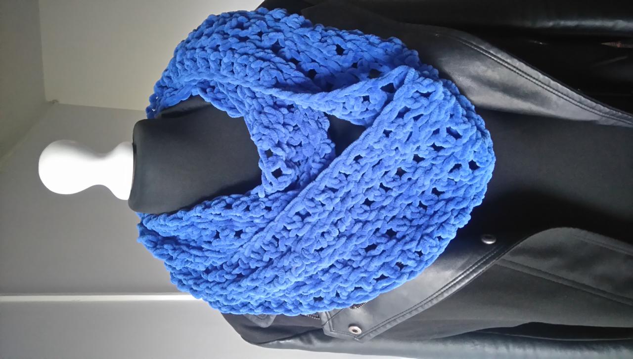 Kobaltowy, dziergany szal typu infinity z grubej włóczki, prezentowany na manekinie z czarnym torsie i białą głową, na tle czarnej skórzanej kurtki.