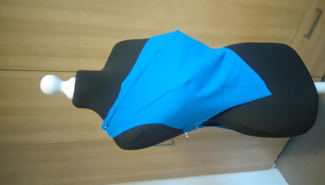 Niebieski materiał drapowany na czarnym manekinie krawieckim w Moszna-Parcela, widoczne szpilki krawieckie, w tle drewniana szafa.