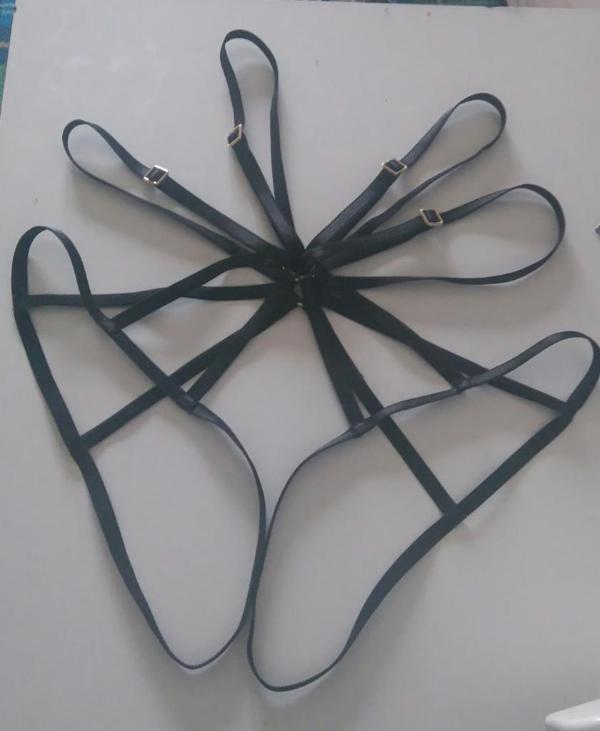 Czarny, regulowany pas do pończoch z metalowymi sprzączkami w kolorze złotym, ułożony na białym tle.