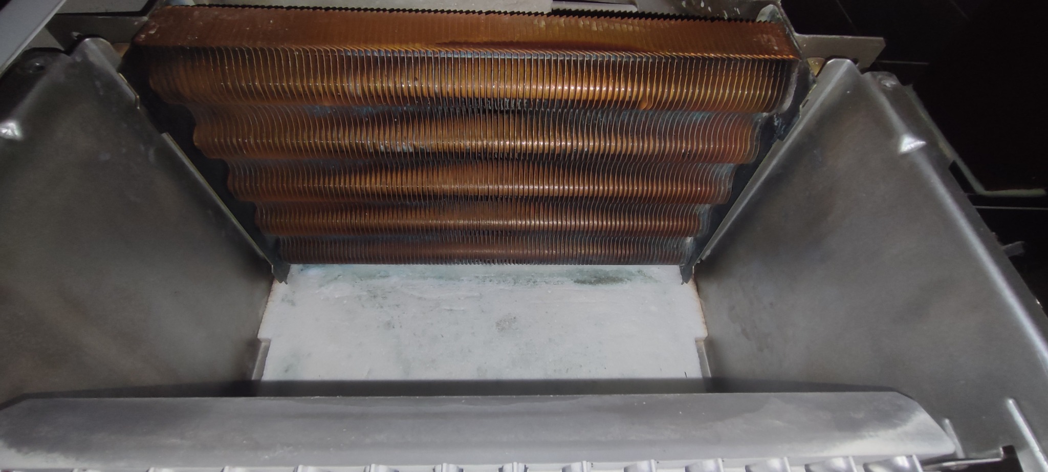 Miedziany wymiennik ciepła wewnątrz obudowy pieca gazowego, widoczne ślady użytkowania i osady. Ujęcie z góry, wnętrze pieca oświetlone.