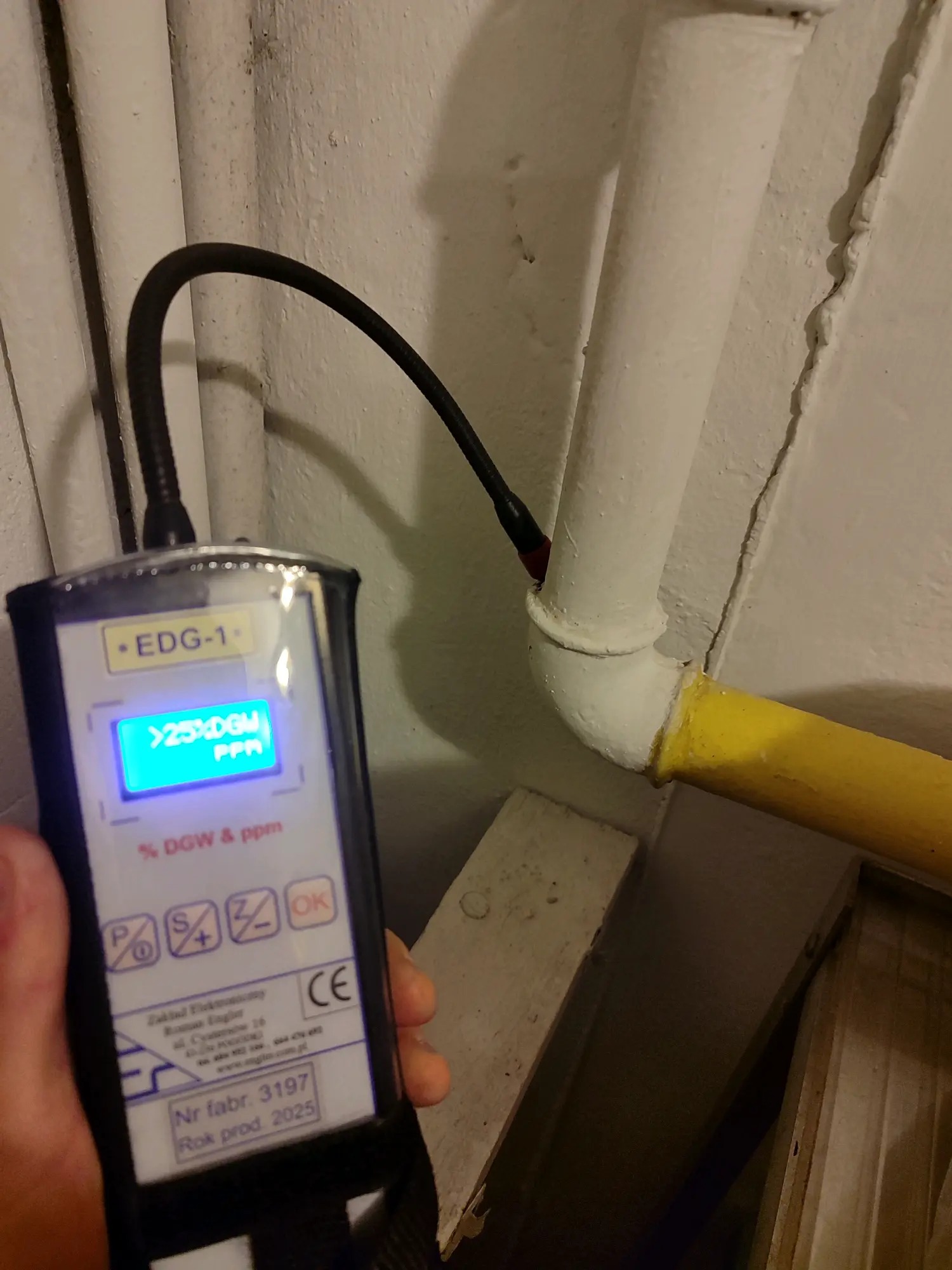 Pomiar stężenia gazu w instalacji detektorem EDG-1. Żółty gazociąg przy ścianie. Urządzenie wskazuje wartość powyżej 25% DGW. Kontrola szczelności instalacji gazowej.