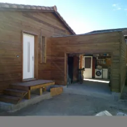 Nowoczesny budynek gospodarczy z drewna z dobudowanym garażem, widoczna pralka i rower wewnątrz.