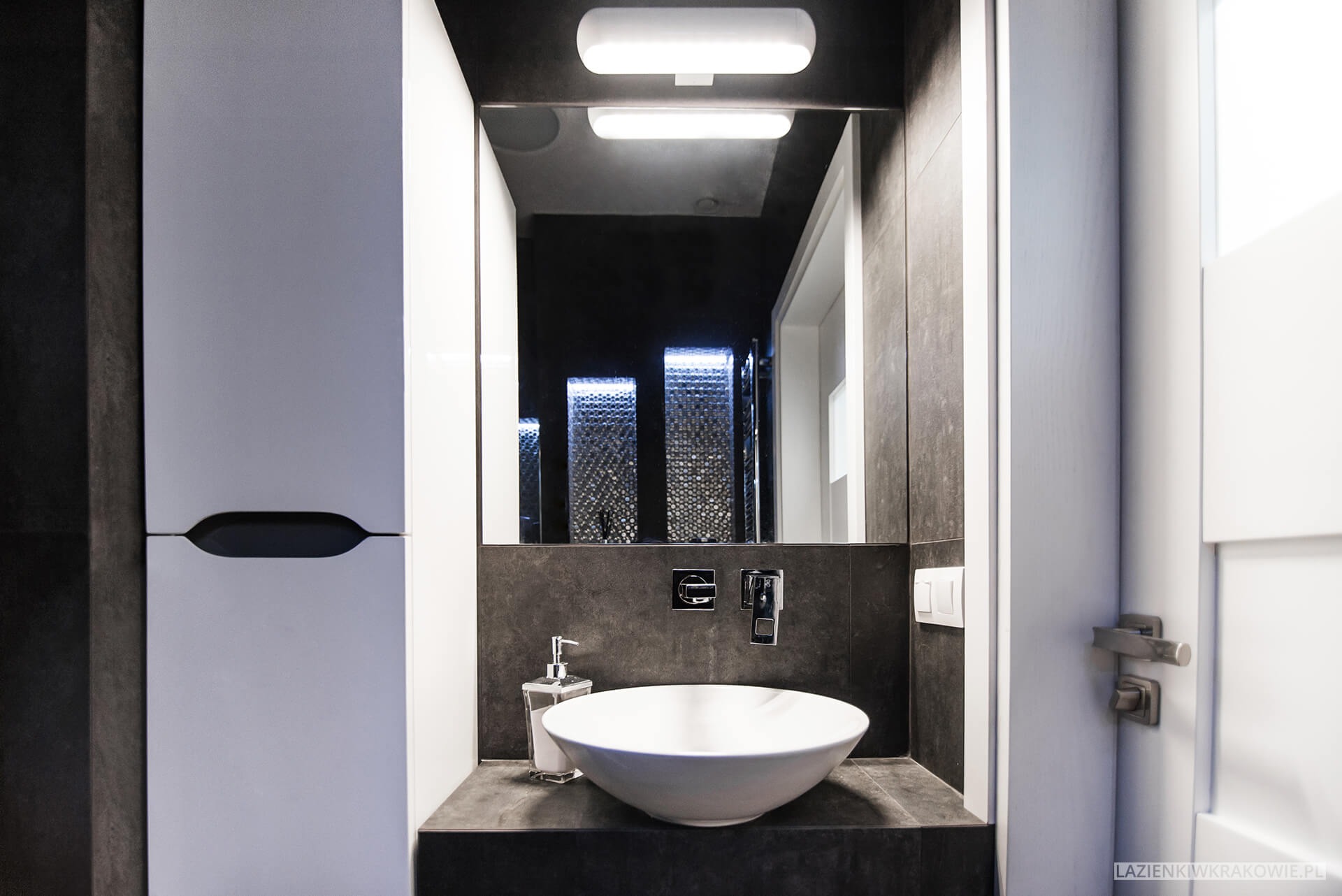 Nowoczesna łazienka z umywalką nablatową w kształcie misy, armaturą podtynkową, lustrem z oświetleniem LED i szafką z minimalistycznym uchwytem w kolorze białym i grafitowym.