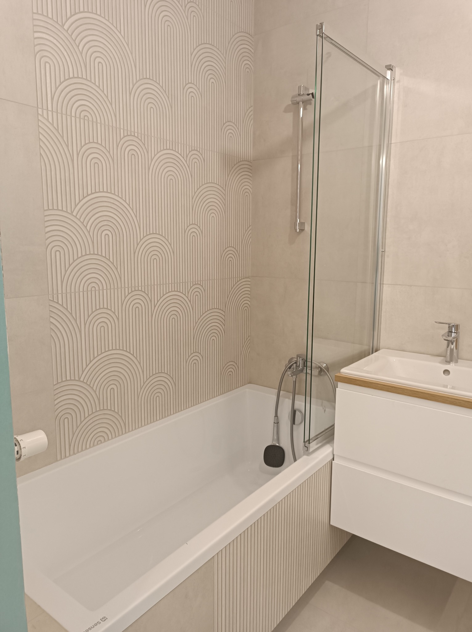 Nowoczesna łazienka z wanną, kabiną prysznicową i umywalką z szafką. Beżowe płytki z geometrycznym wzorem na ścianie. Minimalistyczny design.