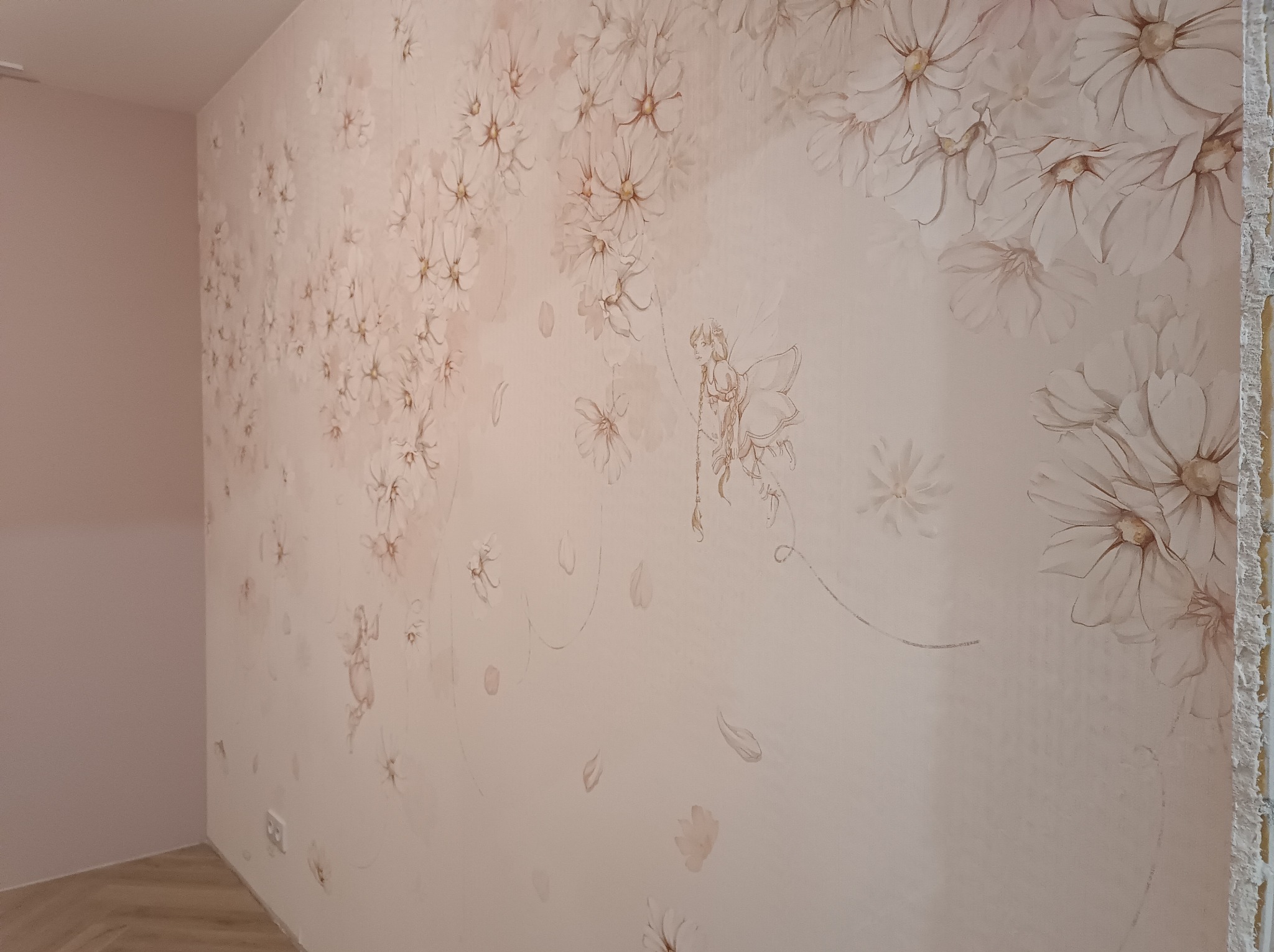 Ściana z delikatnym, kwiatowym wzorem w odcieniach beżu i różu, z motywem wróżki. Widoczny fragment ściany przed wykończeniem, z surowym brzegiem.