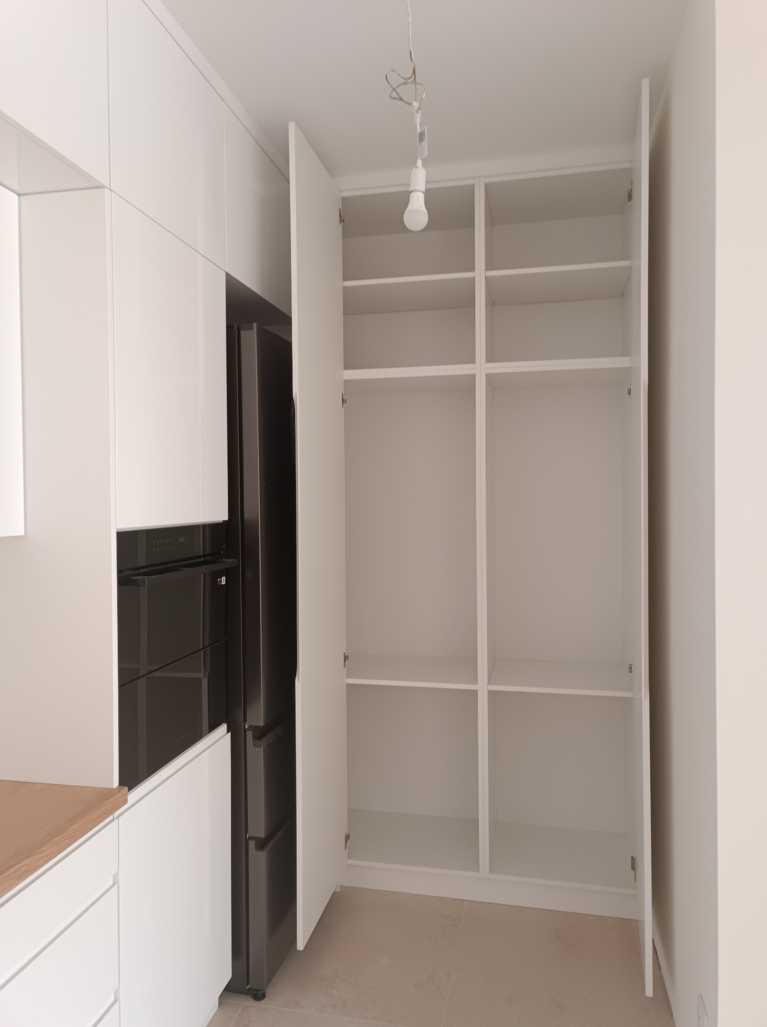 Biała, nowoczesna zabudowa kuchenna z otwartymi szafkami i wbudowanym sprzętem AGD. Minimalistyczny design, jasne wnętrze, widoczna struktura półek.