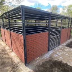 Metalowa konstrukcja z ceglaną podstawą, prawdopodobnie wiata lub zadaszenie, z poziomymi szczeblami, na zewnątrz, na ziemi.