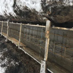 Wykop z deskowaniem i zbrojeniem zalewany betonem, widoczne ślady śniegu na ziemi i skarpie wykopu.