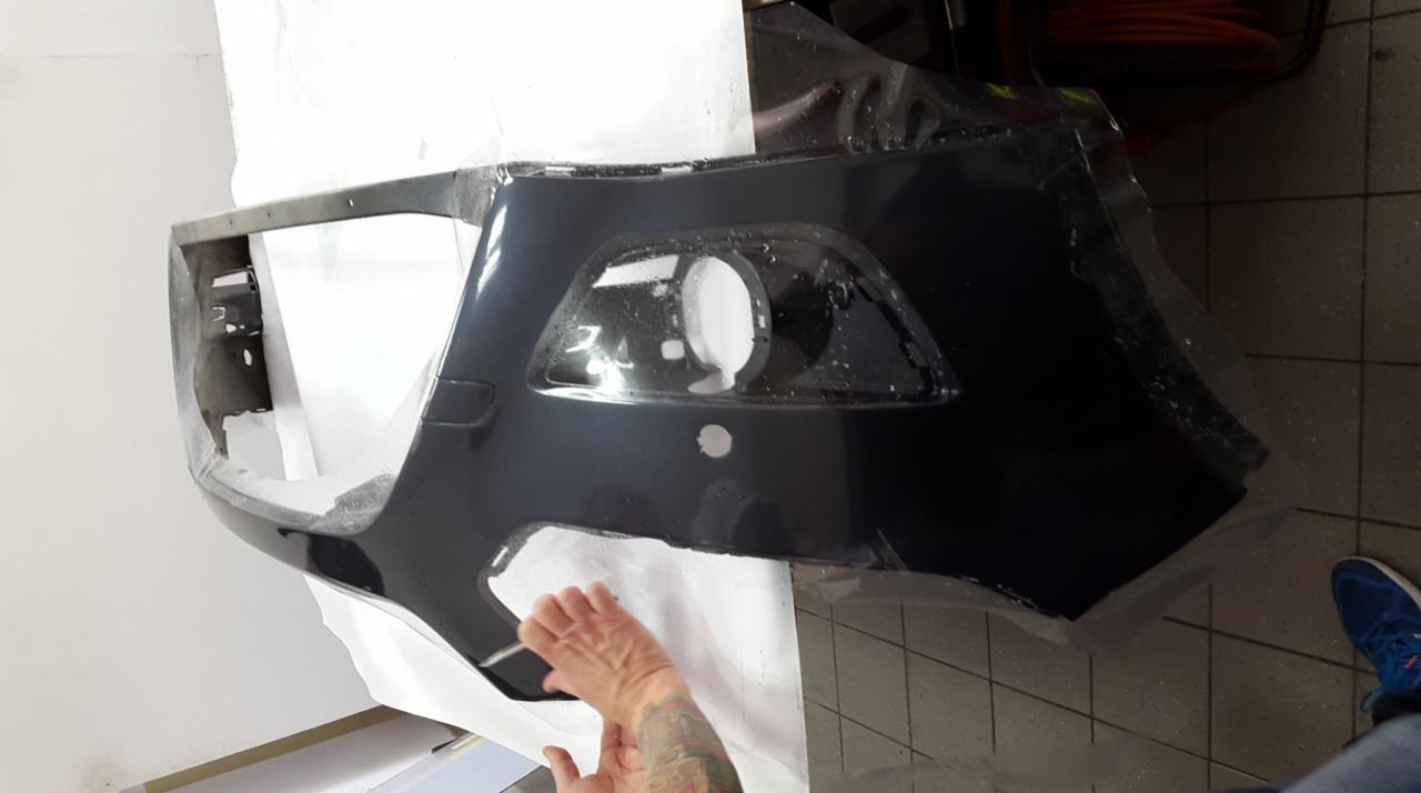 Oklejanie folią ochronną przedniego zderzaka samochodowego, widoczne dłonie pracownika z tatuażami.