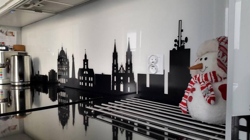 Czarny, wycięty motyw panoramy miasta na białym panelu ściennym w kuchni, z widocznymi gniazdkami elektrycznymi i pluszowym bałwanem