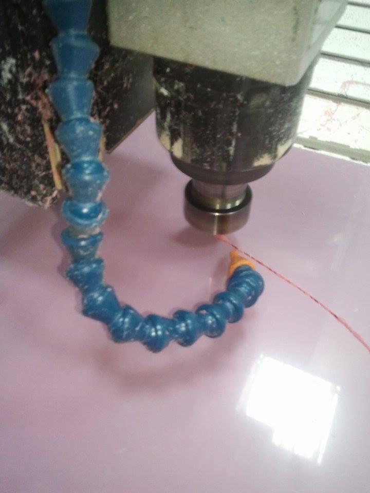 Frezarka CNC w trakcie obróbki różowej płyty, widoczny przewód chłodzenia i wióry.