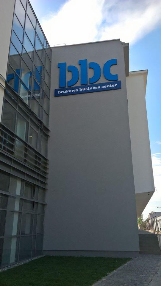 Elewacja budynku biurowego z dużym, niebieskim napisem 'bbc' i 'brukowa business center' pod spodem, widok z dołu.
