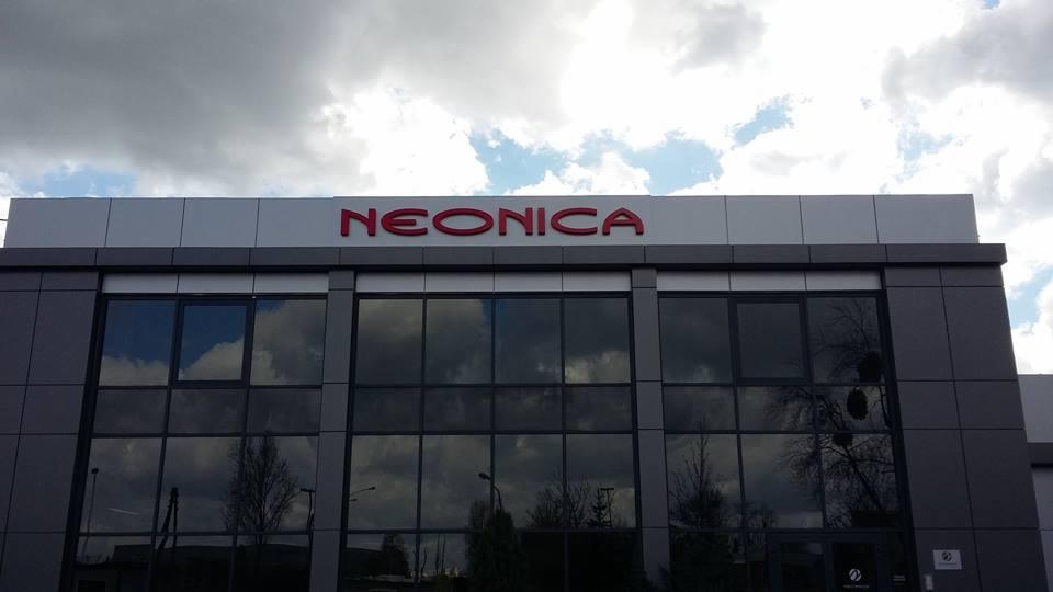 Elewacja budynku biurowego z dużym, czerwonym napisem 'NEONICA' na górze, odbicie chmur w oknach.