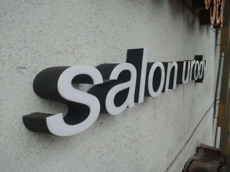 Przestrzenne litery z napisem 'Salon Urody' na szarej, chropowatej ścianie, widoczne z boku pod kątem.