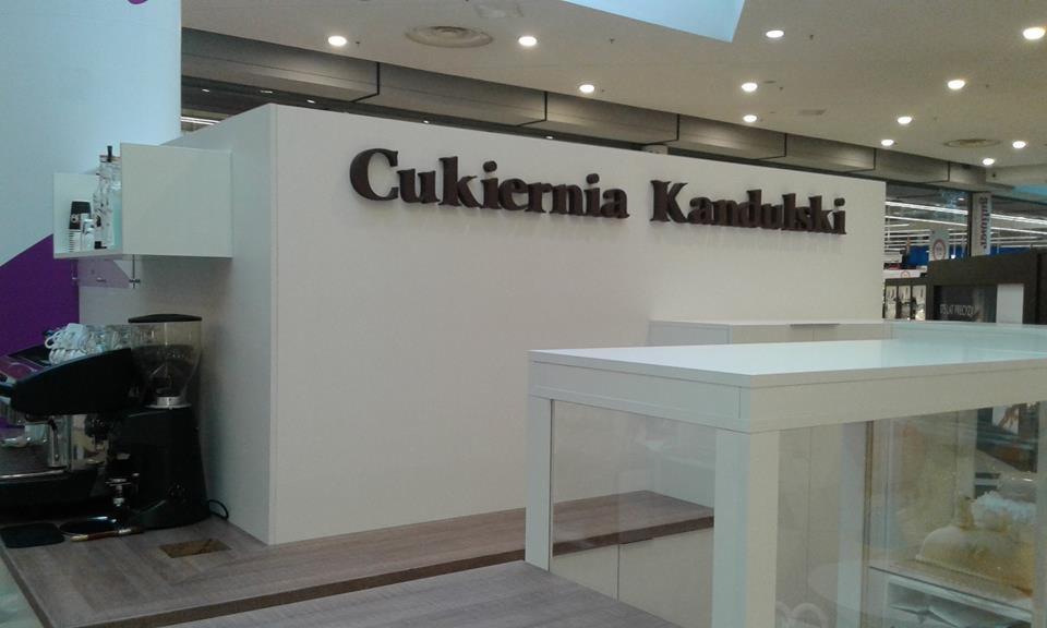Wnętrze cukierni Kandulski z widocznym ekspresem do kawy, ladą i brązowym napisem na białej ścianie w centrum handlowym.