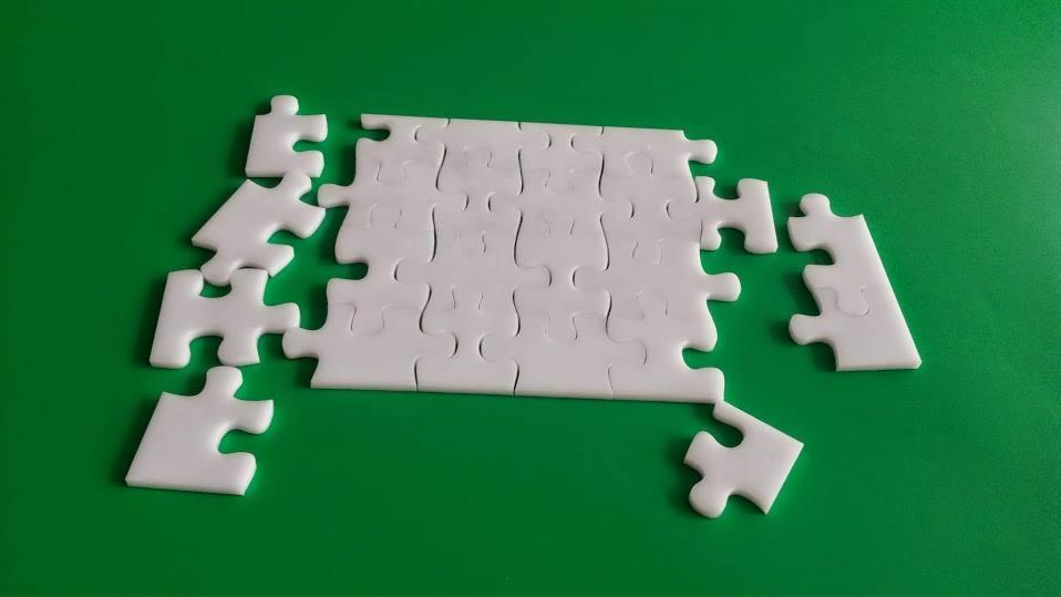 Niedokończona biała układanka na zielonym tle, z kilkoma elementami leżącymi obok ułożonego fragmentu.