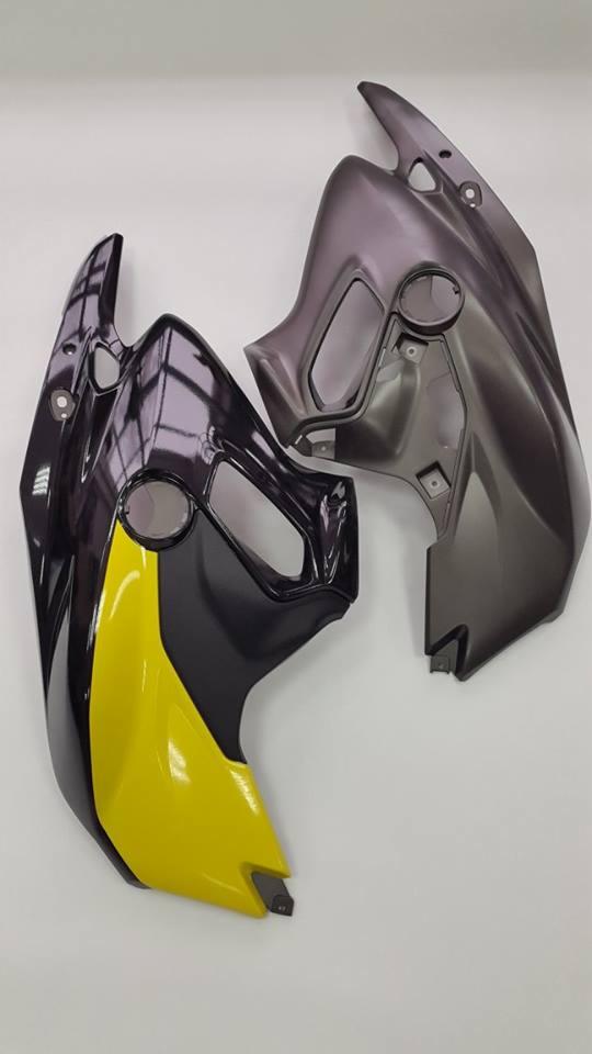 Dwa elementy owiewki motocyklowej: czarno-żółta z połyskiem i szara z matowym wykończeniem, leżące na białym tle.