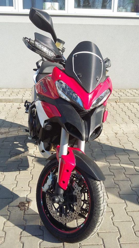 Czerwono-biały motocykl Ducati z elementami z włókna węglowego, zaparkowany na chodniku z kostki, widok z przodu.