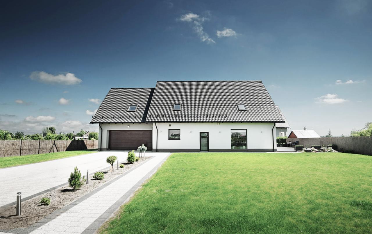 Nowoczesny, parterowy dom z dwuspadowym dachem pokrytym szarą dachówką, z brązową bramą garażową, otynkowany na biało, z zadbanym trawnikiem i podjazdem z kostki.