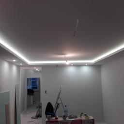 Kamil Kotusiński - Wykończone wnętrze z podwieszanym sufitem i oświetleniem LED, widoczne narzędzia malarskie i drabina, ściany przygotowane do dalszych prac wykończeniowych.