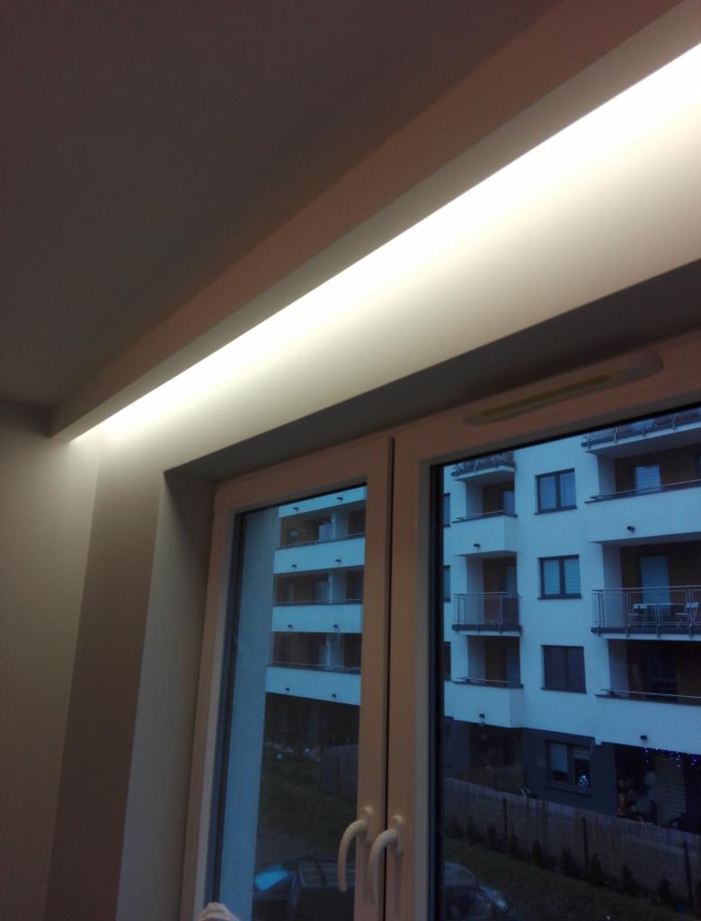 Wnęka okienna z zamontowanym oświetleniem LED, widok na budynek mieszkalny za oknem.