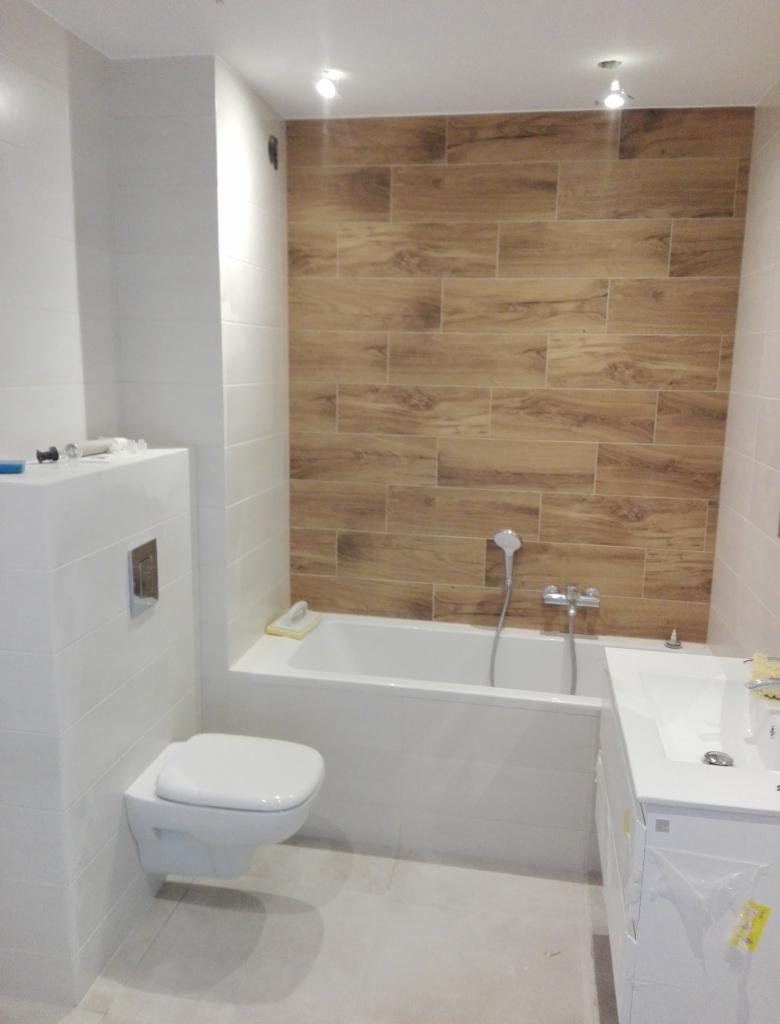 Wykończona łazienka z drewnopodobnymi płytkami na ścianie, białą armaturą i oświetleniem punktowym.