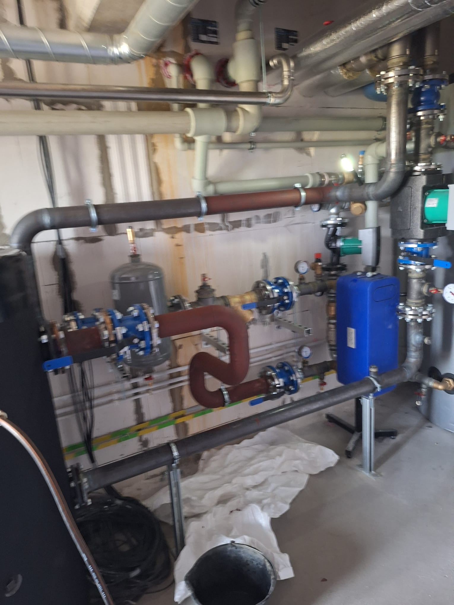 Złożona instalacja grzewcza z rurami miedzianymi i stalowymi, zaworami, manometrami i zbiornikiem wyrównawczym, zamontowana w pomieszczeniu technicznym.