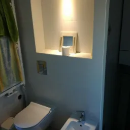 Nowoczesna, minimalistyczna łazienka z podwieszaną toaletą i bidetem, wnęka ścienna z dekoracjami podświetlona punktowym światłem.