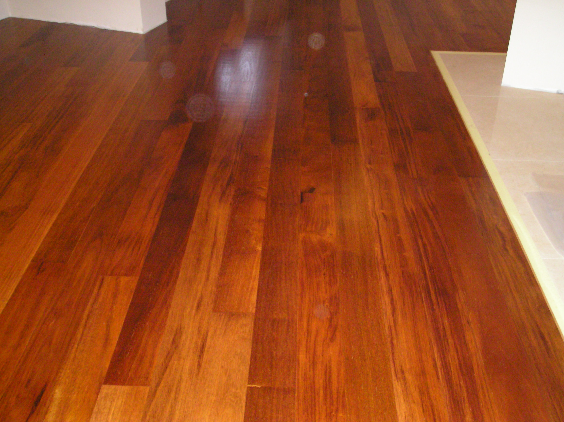 Wykończona podłoga z ciemnego drewna z widocznym fragmentem białej ściany i jasnej podłogi w sąsiednim pomieszczeniu, oddzielonych listwą.