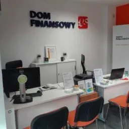 Wnętrze biura Dom Finansowy z biurkami, krzesłami, komputerami i materiałami informacyjnymi, logo firmy na ścianie i baner reklamowy w tle.