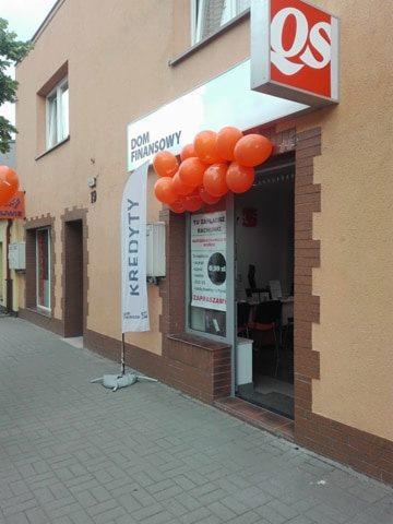 Fasada budynku 'Dom Finansowy' ozdobiona pomarańczowymi balonami, flaga z napisem 'Kredyty' stoi przed wejściem, szyld z logo firmy na górze.
