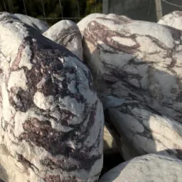 Białe otoczaki z brązowymi żyłkami, ułożone w pryzmę, oświetlone słońcem.