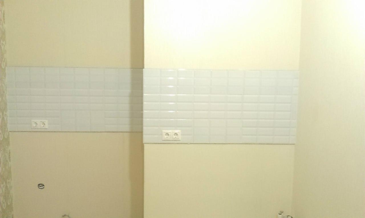 Fragment ściany z ułożonym pasem białych, prostokątnych płytek ceramicznych, z widocznymi gniazdkami elektrycznymi, na tle pomalowanej ściany w odcieniach kremu i beżu.