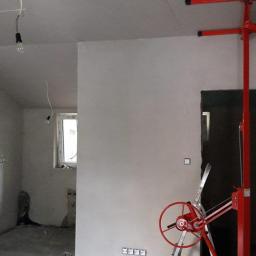 MalHus Szpachlowanie Natryskowe, Malowanie, GK Zabudowy,Poddasza - Wnętrze w trakcie prac wykończeniowych: zamontowane płyty kartonowo-gipsowe na suficie, ściana wstępnie wyrównana, widoczny podnośnik do płyt oraz profile konstrukcyjne na podłodze.