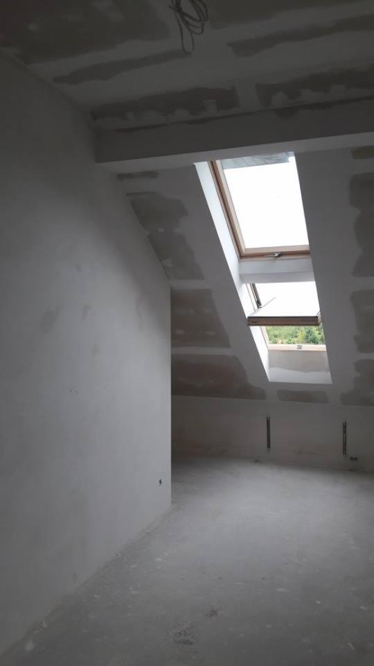 Poddasze w trakcie przygotowania do wykończenia, widoczne płyty kartonowo-gipsowe na ścianach i suficie, szpachlowane łączenia oraz dwa okna dachowe.