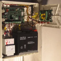 Otwarta obudowa centrali alarmowej Satel Integra 128-WRL z widoczną płytą główną, modułami rozszerzeń, akumulatorem LMRA i transformatorem bezpieczeństwa, zamontowana na ścianie.