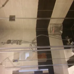 Kabina prysznicowa z chromowanymi okuciami i deszczownicą na tle ściany z płytek w kolorach beżowym i czarnym.