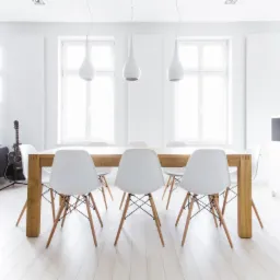 Jasne wnętrze jadalni z drewnianym stołem, białymi krzesłami Eames, trzema lampami wiszącymi w kształcie kropli i gitarą akustyczną w tle.
