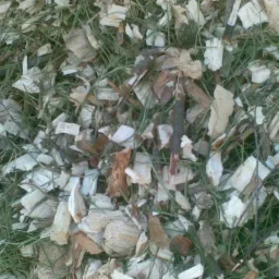 Drobne, jasne kawałki drewna zmieszane z zieloną trawą i suchymi gałązkami, tworzące naturalną ściółkę.