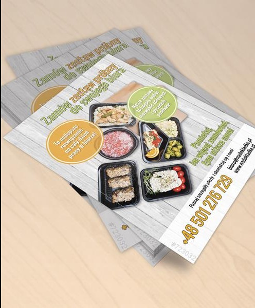 Ułożone ulotki reklamowe z ofertą zestawów obiadowych dla biur, prezentujące różnorodne dania w czarnych pojemnikach na tle imitacji drewnianych desek.