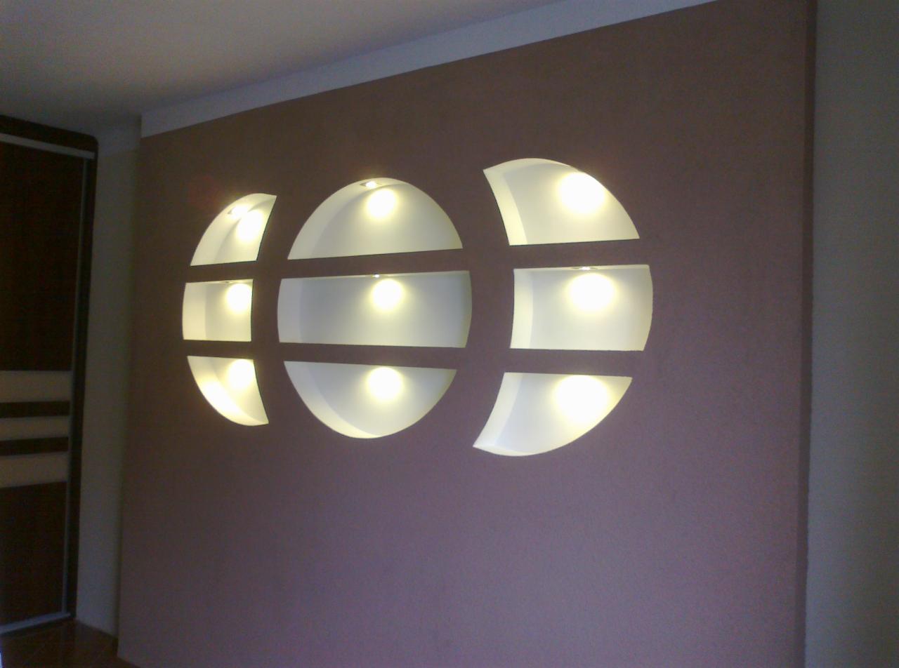 Dekoracyjna ściana z wnękami w kształcie półksiężyców, oświetlonych punktowo, na gładkiej, brązowej ścianie w pokoju.