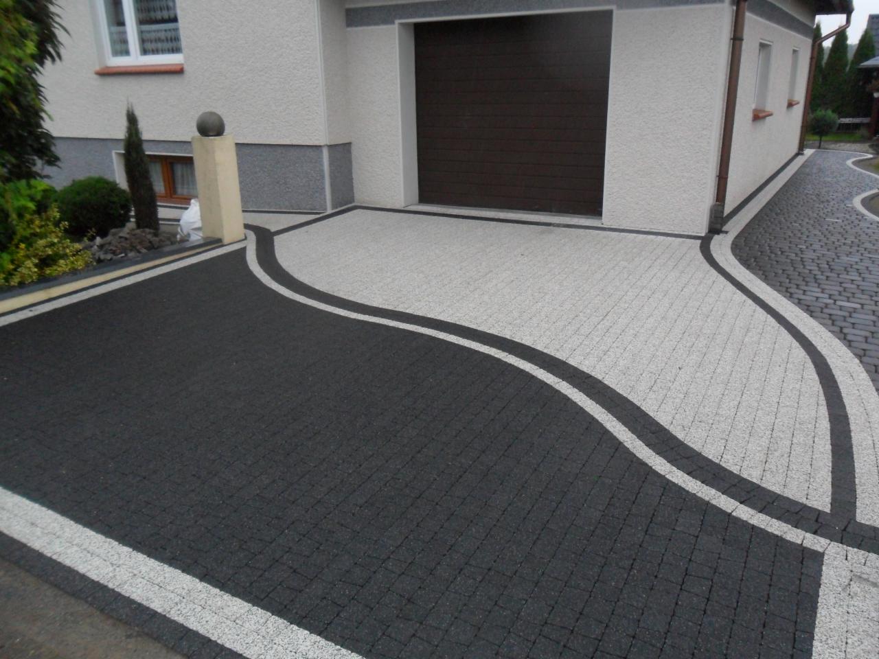 Czarno-szara nawierzchnia z kostki brukowej ułożona we wzór z falistą linią podjazdu do garażu, widok z góry.