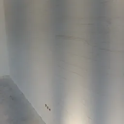 Ściana z dekoracyjną fakturą w odcieniach bieli i beżu, widoczne gniazdka elektryczne, surowy beton na podłodze.