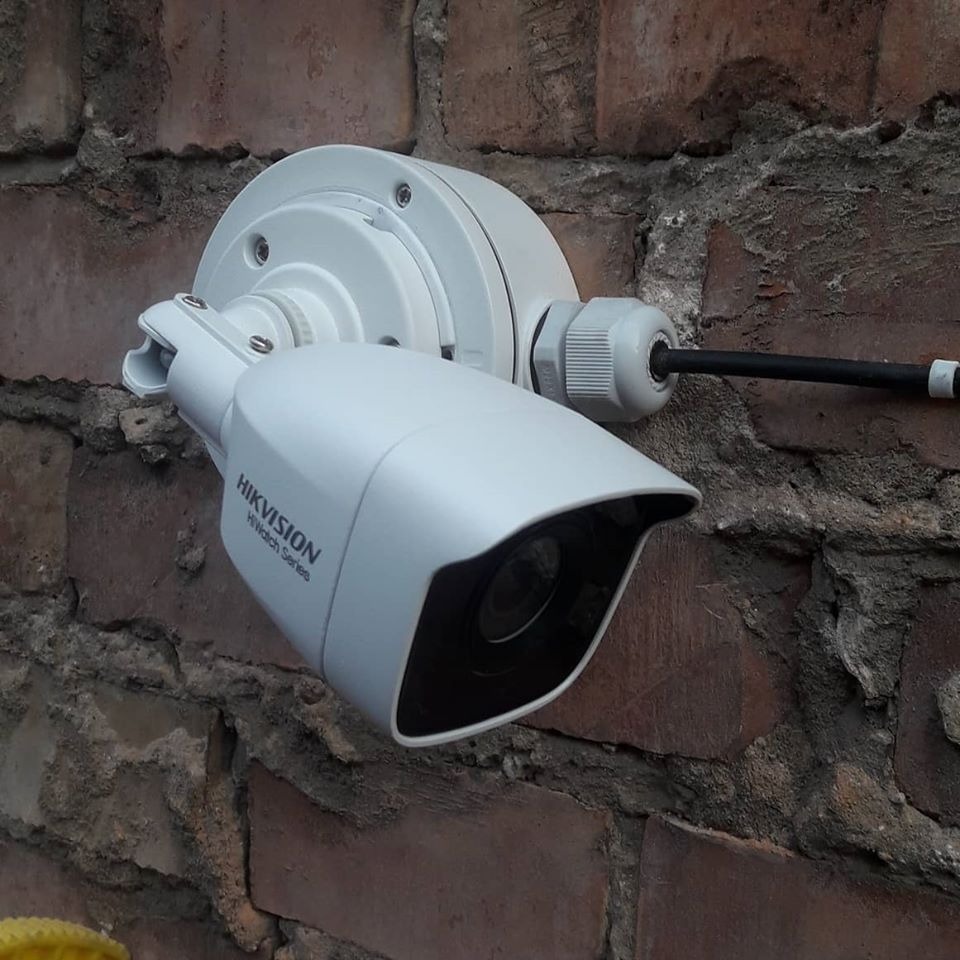 Kamera przemysłowa Hikvision HiWatch Series zamontowana na ceglanej ścianie, kabel podłączony do puszki instalacyjnej.