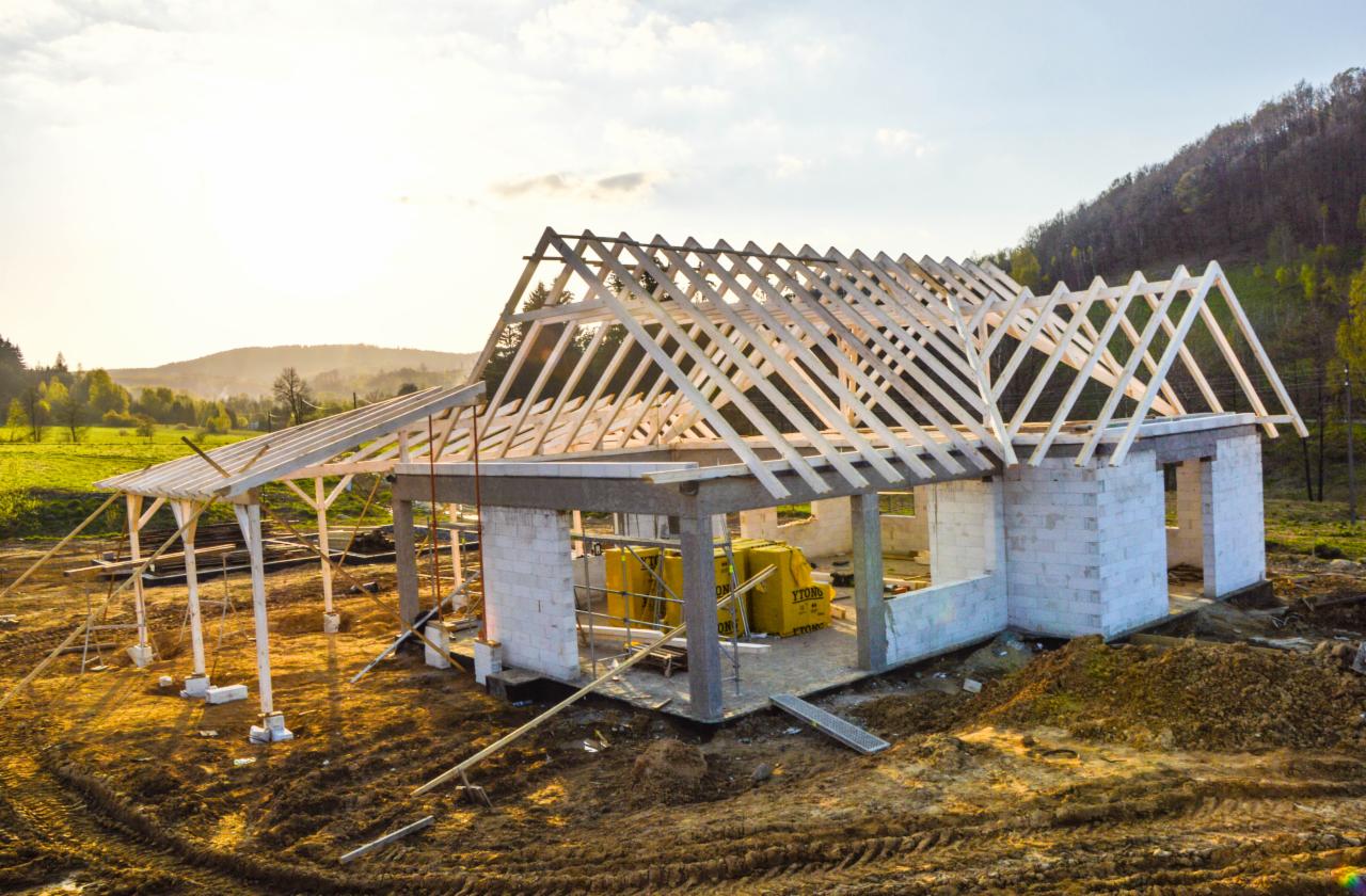 Budowa domu jednorodzinnego z betonu komórkowego w Zagórzu Śląskim, widoczna konstrukcja drewniana dachu i ocieplenie Ytong wewnątrz budynku, krajobraz zalesionych wzgórz w tle.